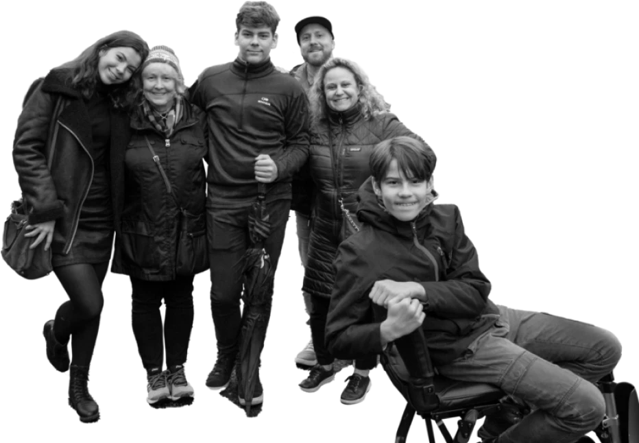 Group family photo of six people, one of whom is seated in a wheelchair and diagnosed with LGMD2I/R9, all smiling and standing closely together